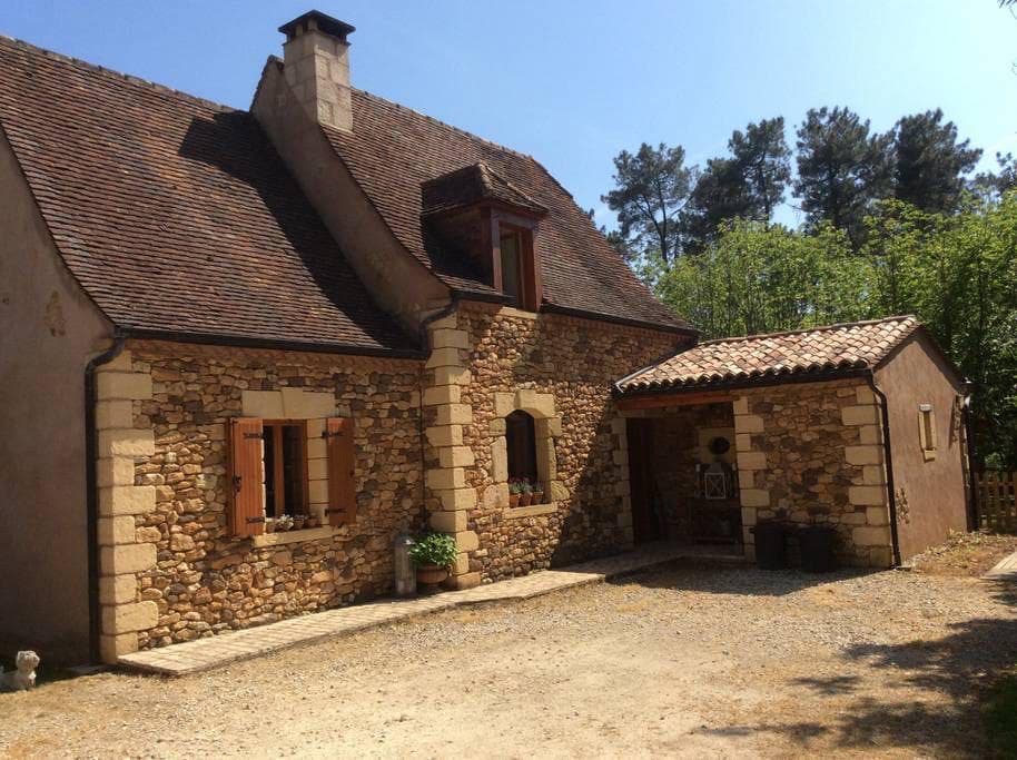 Huis van natuursteen met rode luiken in de zon, omgeven door bomen